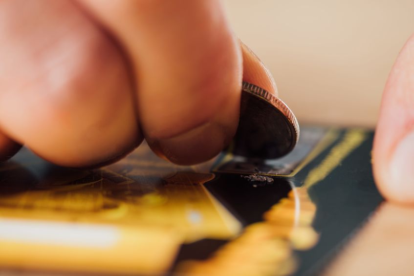 A hand with a quarter is scratching off a lottery ticket